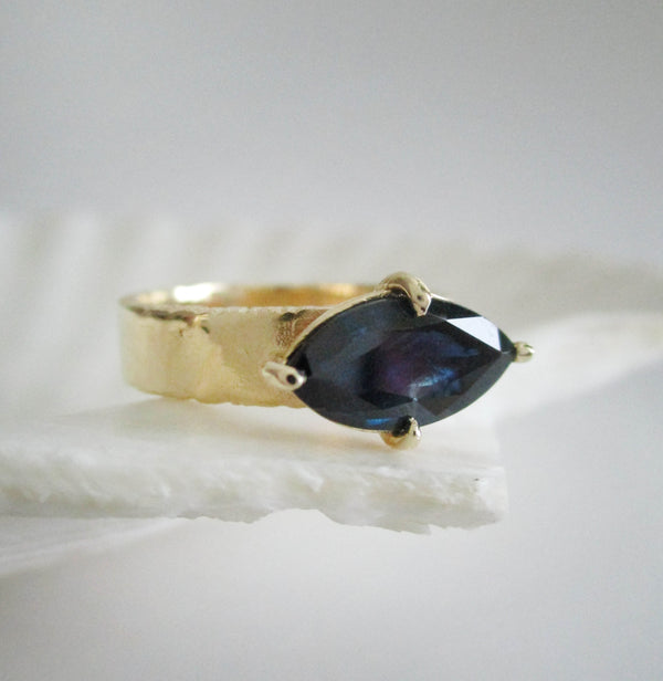 14K yellow gold 5mm ring with 4 prong marquis sapphire center on a white background