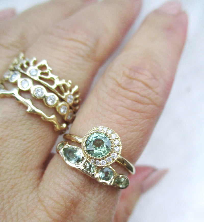 14K gold ring with green sapphires on the hand against a white background