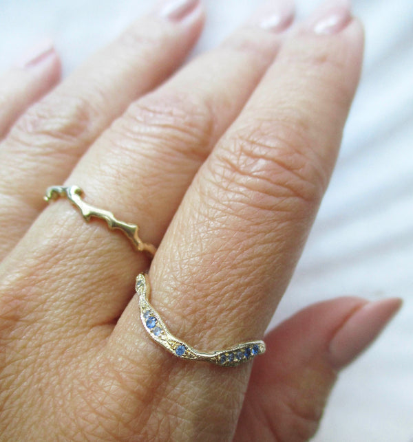 14K gold curved stacking ring with blue sapphires on a hand against a white background