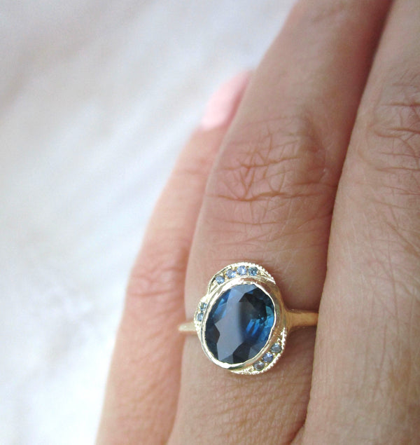 14K gold ring with an oval sapphire gemstone on a person's finger against a white background