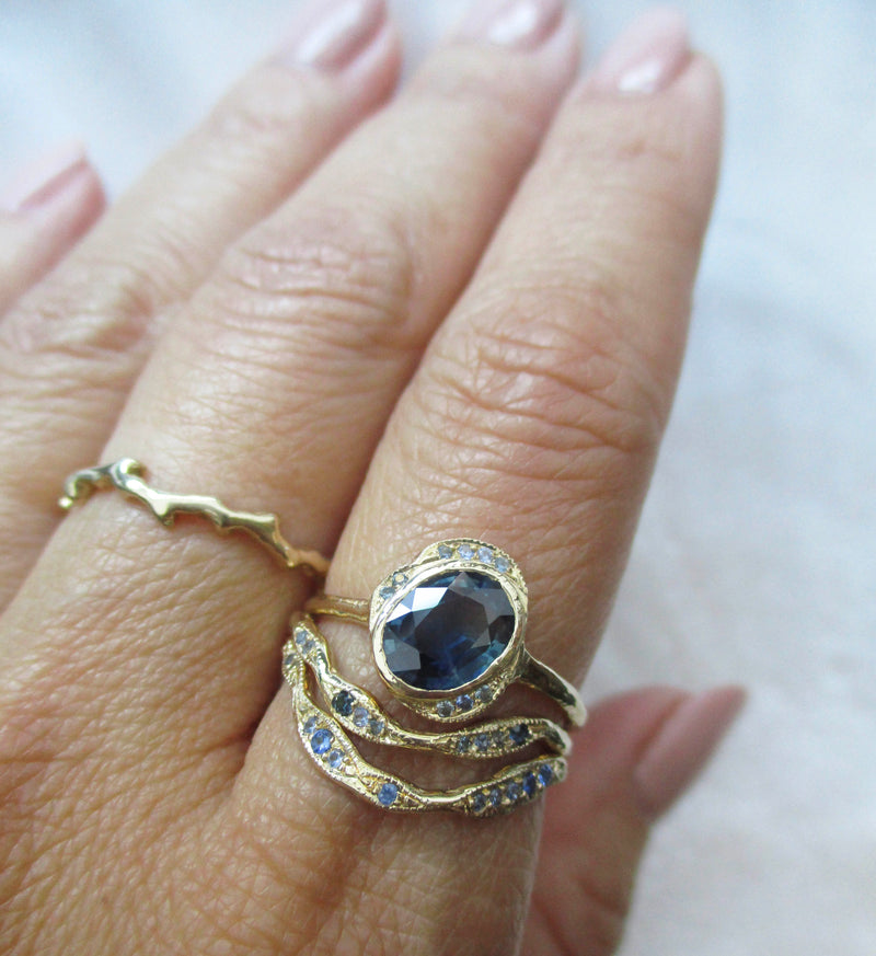 Gold ring stack with sapphires on a hand against a light background