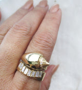 Gold shell-shaped ring with diamond accents on a finger paired with a baguette diamond ring against a white background