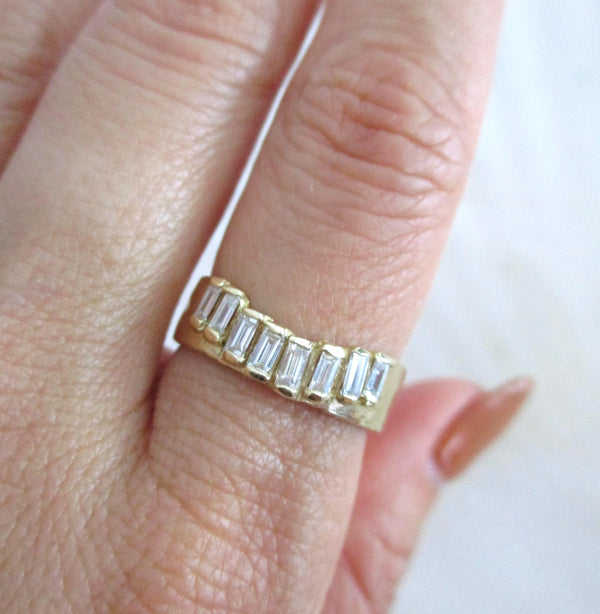 14K gold ring with baguette diamonds on a finger against a neutral background
