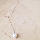 14K gold necklace with pearl on table.