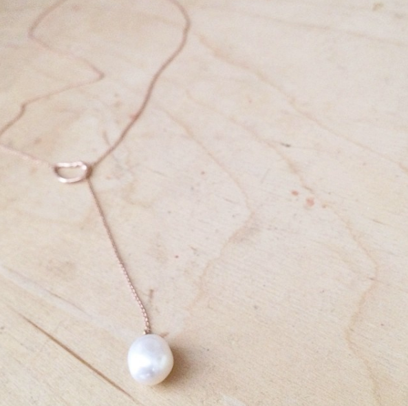 14K gold necklace with pearl on table.